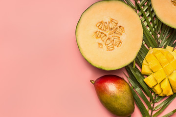 healthy food, tropical fruits, mango, melon on a monstera leaf with smoothies on a pink background, space for text flat lay