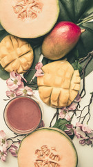 concept of a vegetarian, healthy food, fresh sliced mango and melon with smoothies, with flowers and leaves of monstera, top view flat lay