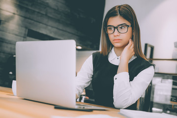 The woman in glasses working with the modern laptop at the table