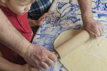 Obraz na płótnie Canvas dad teaches his son to roll out dough