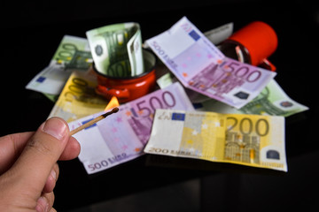 Burning euro banknotes with a matches. Reflection of euro banknotes on a black glass