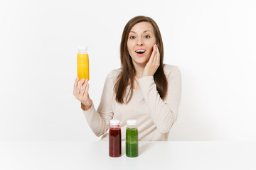 Young woman at table with green, red and yellow detox smoothies in bottles isolated on white background. Proper nutrition, vegetarian drink, healthy lifestyle, dieting concept. Area with copy space.