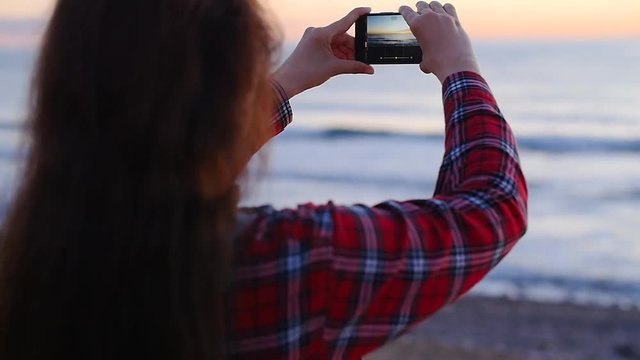 Young woman taking photos on beach during sunset or sunrise