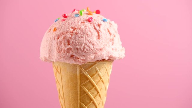 Ice cream. Strawberry or raspberry flavor icecream in waffle cone rotated over pink background. Sweet dessert decorated with colorful sprinkles closeup. 4K UHD video footage. 3840X2160