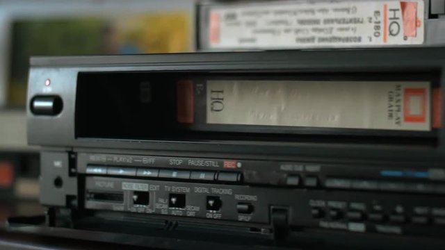 The hand takes a videocassette, inserts it into the video player and pushes the play
