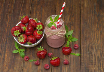 Pink strawberry and raspberry smoothie in a mason jar glass with straw and scattered berries