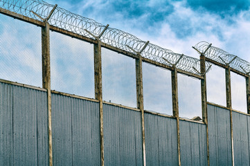 Old high metal fence with barbed wire at the border. Vintage style.