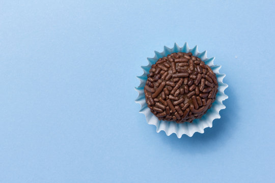 Brigadeiro is a chocolate truffle from Brazil. Cocoa and sprinkles of chocolate. Children birthday party sweet. Top view of candy on blue background.