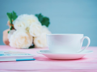 Romantic background with cup of tea or coffee, rose flowers and book over light pink wooden table
