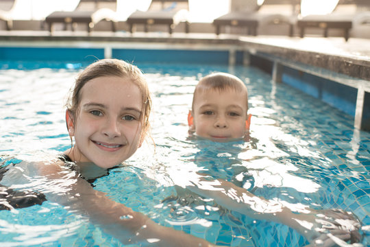 Portrait of positive cute kids with wet hair sitting in warm water of swimming pool and relaxing together