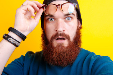 It's incredible! Close up portrait of young bearded man touching the spectacles and keeping his mouth open over yellow background