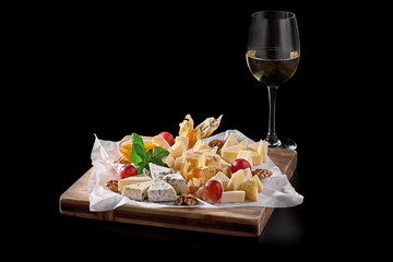 a glass of white wine and a variety of cheeses, nuts and dried fruits on a black background. cafe, pub-menu, the concept of food. copy the place.