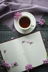 Background with flowers and cup on the purple fabric, notebook