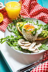 Tasty sandwich with avocado and egg, arugula on white tray on blue wood background. breakfast
