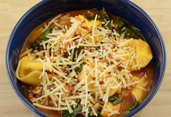Cheese tortellini tomato stew soup with spinach and sausage in blue bowl with shredded cheese on top