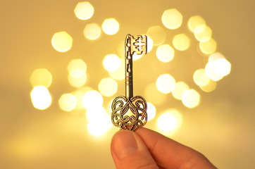 Love is the key. Womans hand holding the key on abstract blurred heart of lights
