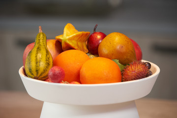 Ripe tropical fruits in a white dish. A plate of tropical fruits and a flower vase standing on the kitchen counter. Luxury modern kitchen interior. Healthy lifestyle and diet food concept