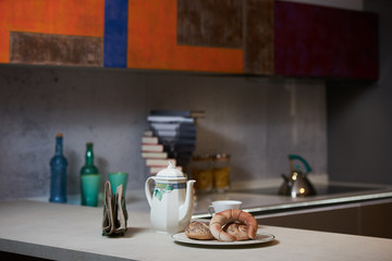 Morning breakfast on a ceramic tray in the modern kitchen interior. Kettle, coffee pot, cup of tea, napkins and croissant on kitchen counter