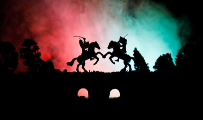 Fototapeta na wymiar Medieval battle scene on bridge with cavalry and infantry. Silhouettes of figures as separate objects, fight between warriors on dark toned foggy background. Night scene.