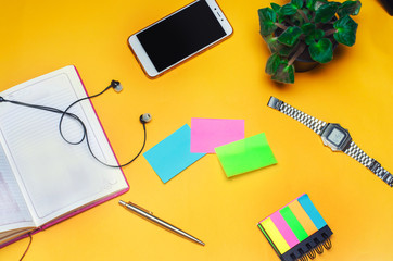working space with a notebook, pen, clock, telephone, headphones on a yellow background. place for text. The working space of a freelancer, journalist, writer. On a bright yellow background. Top view.
