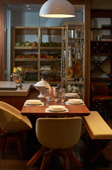 Luxury kitchen dining table setting, glasses, cutlery and wine in ice bucket. Modern kitchen interior with clean white plates, glasses and cutlery on wooden table