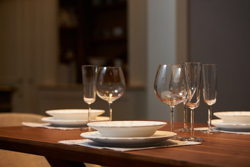 Luxury kitchen dining table setting, glasses, cutlery and wine in ice bucket. Modern kitchen interior with clean white plates, glasses and cutlery on wooden table