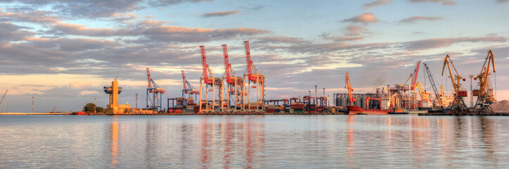 Loading grain to the ship in the port. Beautiful view of the ship, cranes, and other infrastructures of the port on sunset
