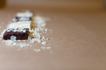 Snack chocolate protein bars with different flavors in the context of sprinkle rice flakes on baking paper, Teflon paper. Whey protein powder and chocolate protein bar on wooden background. Text space