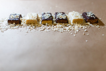 Snack chocolate protein bars with different flavors in the context of sprinkle rice flakes on baking paper, Teflon paper. Whey protein powder and chocolate protein bar on wooden background.