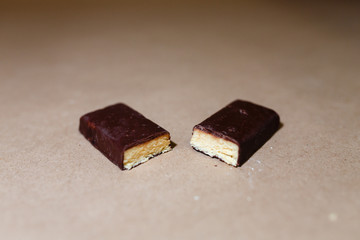 Closeup protein bar in the cut on the baking paper, Teflon paper, Diet snacks, sports nutrition. Whey protein powder and chocolate protein bar on wooden background.