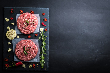 Top view of raw burger cutlets from minced ready for cooking with rosematy twig, garlic and chili on a slate board, background cooking