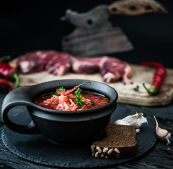 Borsch traditional Ukrainian and Russian soup in ceramic bowl with rye bread, chilly paper and garlic. Meat and butcher knife on the background.
