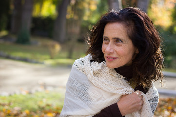 Dazzling mature woman keeping warm with white shawl over her shoulders in the park. Fall season fashion, glamour concept