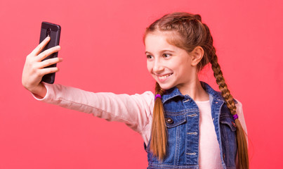 Pretty young girl with braided hairstyle smilig while making selfie over bright pink wall