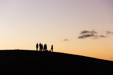 Fototapeta premium Group of friends enjoying nice sunset on top of Maspalomas sand dunes in Canary Islands. Adventure explorers walking on a different planet concept