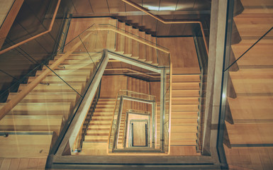 Spiral staircase from above with parquette floor. Square shaped stairs going downwards creating layers from each floor.