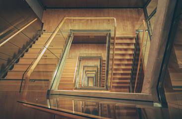 Spiral staircase from above with parquette floor. Square shaped stairs going downwards creating layers from each floor.