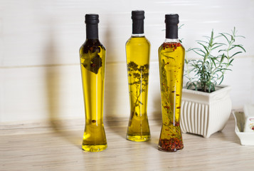 Three bottes of  olive oil with spieces, rosemary, pepper, oregano, allspice, bay leaf and pot with rosemary  on the kitchen table. Selective focus.