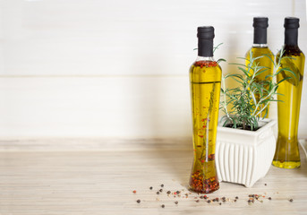 Three bottes of  olive oil with spieces, rosemary, pepper, oregano, allspice, bay leaf and pot with rosemary  on the kitchen table, colorful pepper seeds in the foreground. Selective focus.