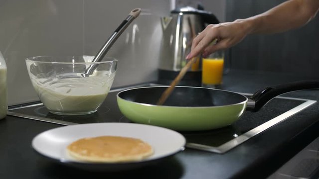 Close-up female hand flipping pancake on frying pan. Woman cooking tasty pancakes for breakfast for family at home.