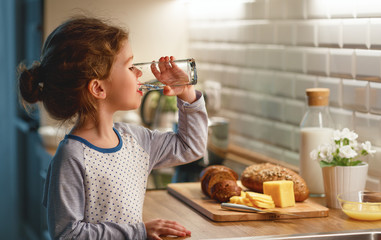 child girl is drinking water in  kitchen at home