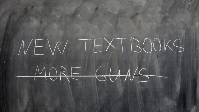 “New textbooks, no more guns” sign written by a child on a chalkboard