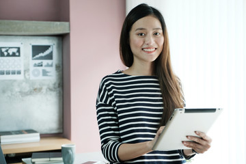 Fototapeta premium Young asian businesswoman using tablet with smiling face, positive emotion, at office, casual office life concept