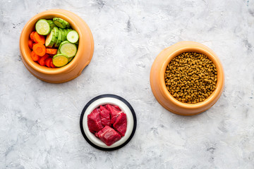 Dry pet food with natural ingredients. Raw meat, cut vegetables zucchini and carrot on stone backgroud top view copy space
