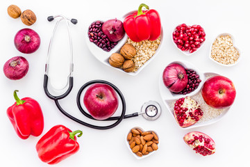 Products good for heart and blood vessels. Vegetables, fruits, nuts in heart shaped bowl near stethoscope on white background top view
