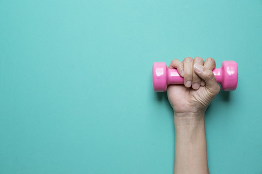 woman hand holding pink dumbbell on green background