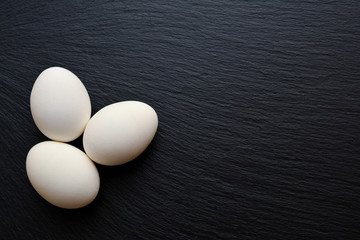 Three white chicken boiled eggs on black slate board, plate, tray.