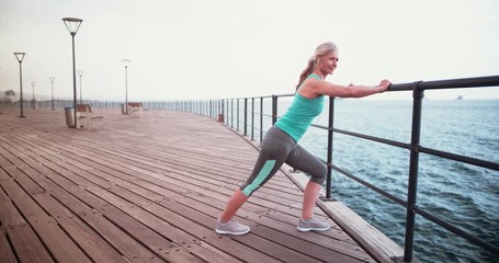 Active senior woman with earphones stretching before jogging at seaside - Powered by Adobe