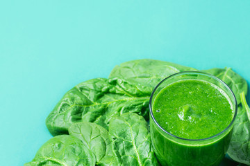 Glass with Green Fresh Smoothie from Leafy Greens Vegetables Fruits. Apples Bananas Kiwi Zucchini Scattered Spinach Leaves on Turquoise Background. Healthy Lifestyle Detox Vitamins. Copy Space