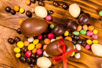 Chocolate easter eggs and multicolored candies on wooden table. Top view